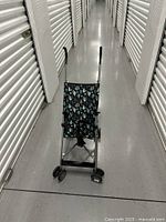 Full view of the umbrella stroller showing the teal raindrop patterned fabric seat and backrest, silver frame, black double front wheels, and black handles in a curved shape.