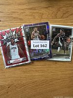 Photo of three Panini Donruss Optic NBA basketball cards including Kawhi Leonard, Spencer Dinwiddie and Dejounte Murray in protective sleeves on wooden surface.