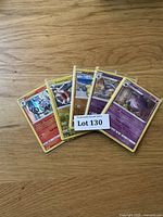 Five Pokémon cards fanned out including Chandelure and Exeggutor visible, with a 'Lot 130' label on top, showing a mix of colors and card types.