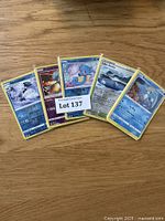 Five Pokémon cards displayed face-up on a wooden surface including Abomasnow, Radiant Greninja, Horsea, Lugia Aqua, and one other.