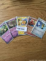 Five Pokémon cards shown fanned out on a wood surface with a label reading 'Lot 141'. Highlights include Misdreavus, Spiritomb, Pikachu, Cramorant, and Sobble cards.