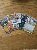 Five Pokémon cards fanned out on wood surface, including Silicobra, Skeleidogre, Zangoose, Crabrawler, and Zweilous with a 'Lot 143' auction tag visible.