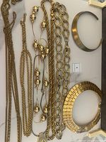 Top view of multiple gold-tone necklaces and collars laid out on flat surface showing variety of styles and designs including chunky links, large beads, twisted ropes, and a bold collar necklace.