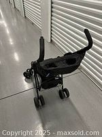 Back view of the stroller showing the handlebar and rear storage basket in a storage unit hallway.