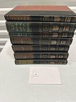 Stack of 8 hardcover leatherette volumes with gilt titles and volume numbers. Titles visible include Aristotle, Plato, and others. Books arranged stacked on a white surface.