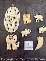 Photo showing all 7 carved pendants and charms including dragon medallion, elephant pendants, and tusk pendant arranged on black background with lot number.