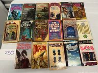 Top-down view of 20+ vintage sci-fi and fantasy paperback books laid out on a white table, showing front covers with various colorful and illustrated designs.