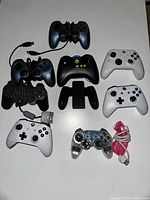 Top view of 10 mixed video game controllers including Xbox and PlayStation models, cables mostly wrapped