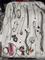 Wide view of assorted necklaces, bracelets, pendants, and a wristwatch on white background.