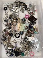 Top view of a mixed lot of various costume jewelry items including bracelets, earrings, pendants, rings, and beads, mostly silver-toned with some colorful accents.