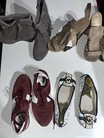 Top-down view of five pairs of women's shoes including boots, sandals, sneakers, and flats laid out on a white surface.