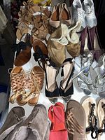 Downward view of 13 pairs of women's mixed shoes laid out on a white surface showing various styles including sandals, flats, boots, and heels in different colors and materials.