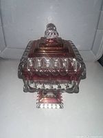 Front view of the candy dish with the lid on, showing the clear and ruby red glass with faceted details and knob handle.
