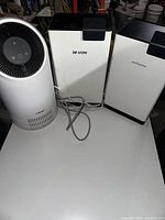 Wide view of three units: one air purifier and two dehumidifiers on white surface.