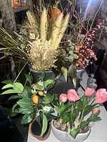 Photo showing a grouping of various artificial plants including pampas grass, eucalyptus, citrus tree, and pink tulips in pots on a table