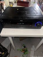 Front view of RCA home theater receiver powered on, showing LINE-IN on digital display and blue-lit volume knob.