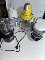Four countertop kitchen appliances shown together: Ninja food processor, Frigidaire blender, Baby Brezza food processor, Deni chopper.
