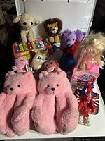 Photo of toys and teddy bears including two large pink teddy bears, small plush animals, a doll, a xylophone, and robot toy.