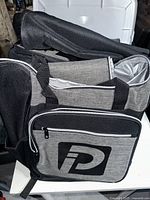 Multiple cooler backpacks stacked, showing the black and gray color scheme and exterior pocket with logo.