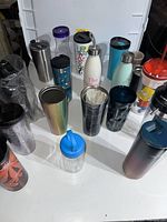 Group photo showing various water bottles and tumblers in different colors and styles, mostly stainless steel and plastic.