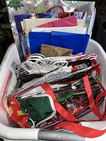 Wide view of bin containing various folded gift bags, many with string handles, and folded sheet wrapping paper visible at back