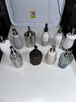 Photo showing all 10 hand soap dispensers arranged on a flat surface, highlighting variety in shape, texture, and color.