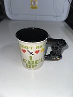 Front view of the mug showing the pixel art text ('Don't Age I Level Up') and hearts and sword graphics with the black controller handle visible.