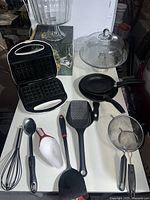 Full lot overview showing all items on a table, including waffle maker, glass cake dish, trifle bowl, pans, and utensils