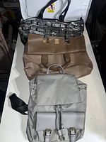 Photo showing three bags: Victoria's Secret tote bag, brown handbag, and gray backpack laid out on a white surface