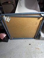 Underside view of folding card table showing plywood base and blue metal legs in folded position.