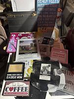 Photo of assorted decorative picture frames and home decor signs in a pile on a surface, showing various colors and texts.