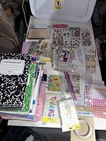 Composition notebooks, assorted stickers, papers, envelopes, cards, and craft supplies arranged on white table.