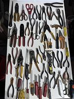 Overall assortment of various pliers, screwdrivers, snips, scissors, files, and cutting tools arranged on a white surface