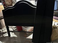 Black full size bed frame headboard in a storage area with various boxes and storage bins around it.