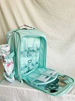 Front view of aqua picnic backpack with cooler pocket and inside compartment visible showing glasses and cutlery.