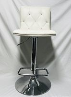 Front angle view of white cushioned bar stool showing tufted diamond button design on backrest and seat, chrome pedestal base and footrest.