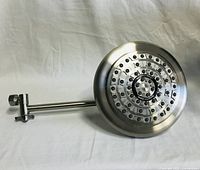 Photo showing large round stainless steel shower head with multiple spray nozzles and swivel arm attachment