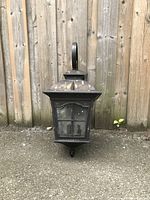 Front view of the black metal porch light fixture showing glass panes and square base mounted on a concrete surface.