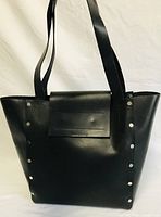 Black leather tote bag photographed from front with visible rivet details on sides and leather patch on front.