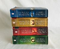 Stack of four George R.R. Martin hardcover books from the series A Song of Ice and Fire, spines facing outward showing titles: A Game of Thrones, A Clash of Kings, A Feast for Crows, A Storm of Swords.