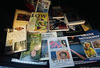 Photo of 14 assorted pre-owned books including photography, travel, fitness, and cookbooks arranged on a dark surface.