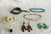 Photo showing assorted costume jewelry laid out on white fabric background, including bracelets, necklaces, earrings, and a ring.