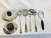 Top view of five stainless steel kitchen utensils and two pot lids on white background