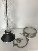 Photo of black metal hanging lamp wrapped in plastic, stainless steel round cylinder ceiling light with frosted glass, and stainless steel three-bulb ceiling light fixture.