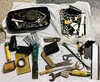 Overview of the small hand tools, brass fittings, metal plates, and hardware components spread on a white cloth.