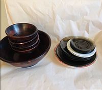 Photo showing large wooden plate with stacked smaller wooden bowls on top, highlighting wear and chipping on larger plate.