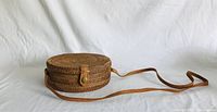 Full side view of the round rattan shoulder bag with leather strap and snap button closure.
