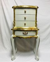 Front view of the French Baroque Rococo style commode featuring four drawers, gold leaf trim, and curved legs on a light painted base.
