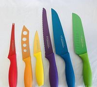 Front view of six assorted colored Tomodachi cutting knives with ergonomic handles laid flat on white background.
