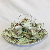 Front view of the mini tea set on plate showing teapot, cups, saucers, sugar bowl, and creamer with floral and butterfly pattern.
